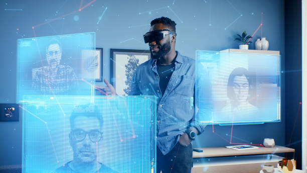 man wearing VR goggles at online business meeting in meta universe cyberspace talking with colleagues over video conference, holographic windows in front of him- expansion of digital into the metaverse